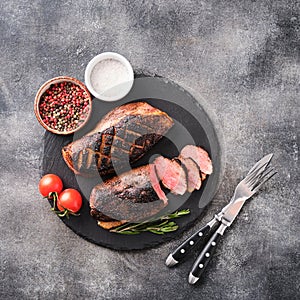 Roasted duck breast on a black slate board with peppers and cherry tomatoes