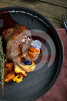 Roasted duck leg with confit pumpkin, closeup. Horizontal top view, top shot. Copy space, wooden background, low key