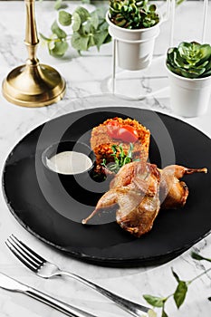 Roasted or fried quail with herbs and rise at black stone plate on light marble background. Healthy sea food, hard light,