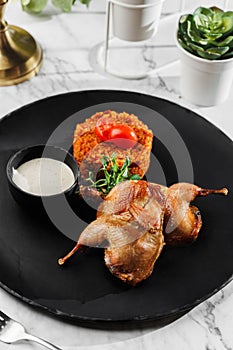 Roasted or fried quail with herbs and rise at black stone plate on light marble background. Healthy sea food, hard light,