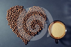 Roasted grains in the shape of a heart and a cup of aromatic coffee on a table
