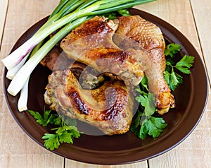 Roasted juicy chicken (legs, winglets) on a clay plate on a light wooden background.