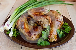 Roasted juicy chicken (legs, winglets) on a clay plate on a light wooden background.