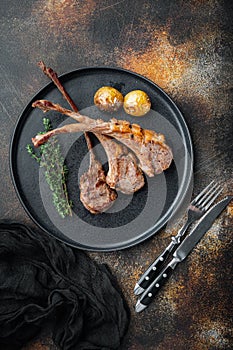 Roasted lamb cutlets ribs with garlic and herbs, on plate, on old dark rustic background, top view flat lay