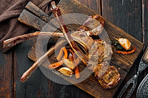 Roasted lamb cutlets ribs with garlic and herbs, on wooden serving board, on old dark  wooden table background, top view flat lay