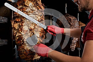 Roasted meat on the bone for the preparation of donors or shawarma. Close-up. The cook cuts the meat fried over charcoal