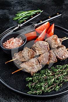 Roasted meat skewers shish kebab and vegetables on a plate. Black background. Top view