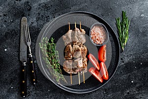 Roasted meat skewers shish kebab and vegetables on a plate. Black background. Top view