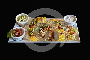 Roasted meat on tortillas and chips with grilled vegetables. The dish includes garlic, avocado and vegetable dip. The food is on a
