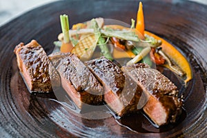 Roasted medium rare wagyu beef served with sour sauce with roasted baby vegetables on stone plate