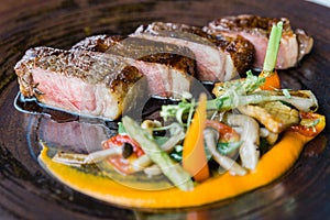 Roasted medium rare wagyu beef served with sour sauce with roasted baby vegetables on stone plate