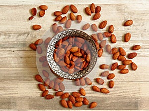 Roasted Natural Almond Nuts Badam in a porcelain bowl. Nuts spilled on bleached oak wood background. photo