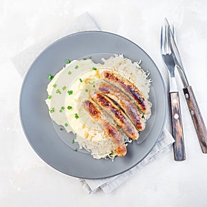 Roasted nuremberg sausages served with sour cabbage and mashed potatoes, on a gray plate, top view, square format