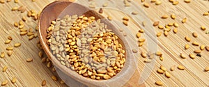 Roasted organic sesame seeds, in wooden spoon on bamboo cutting board