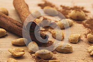 Roasted peanuts with cinnamon sticks, cinamon powder on top of wood table.