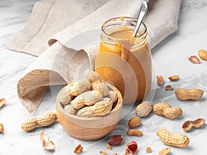 Roasted peanuts in wood bowl and peanut butter in glass jar with napkin on marble table