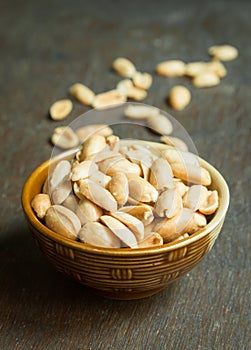 Roasted peeled salted peanuts in rustic bowl on wooden background