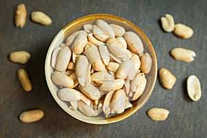 Roasted peeled salted peanuts in rustic bowl on wooden background