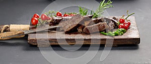 Roasted piece of beef ribeye cut into pieces on a vintage brown chopping board. Delicious steak, close up