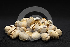 Roasted pistachio nuts in shell on black background, poured roasted peanuts (Pistachio)