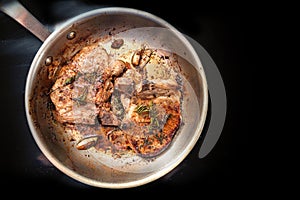 Roasted pork chops with herbs, spices and garlic in a frying pan on a black cooktop, food and cooking concept, copy space, top