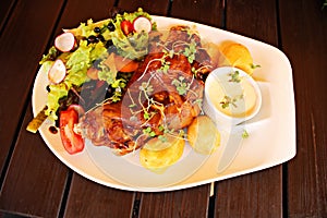 Roasted pork foreshank, boiled potatoes and fresh salad on a white plate