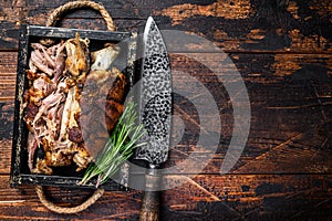 Roasted pork knuckle eisbein meat in a wooden tray with knife. Dark wooden background. Top view. Copy space