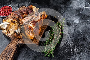 Roasted pork knuckle eisbein on a wooden board with herbs. Black background. Top view. Copy space