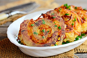 Roasted potato pancakes or draniki with ham slices and green onion on a white plate. Russian stuffed potato pancakes. Closeup