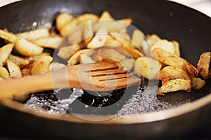 Roasted potatoes close up in a fragrant seasoning in pan in butter with wooden spoon