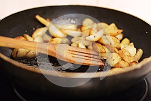 Roasted potatoes close up in a fragrant seasoning in pan in butter with wooden spoon