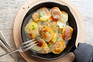 Roasted potatoes slices in iron skillet with herbs. Rustic background, top view. Close up, selective focus