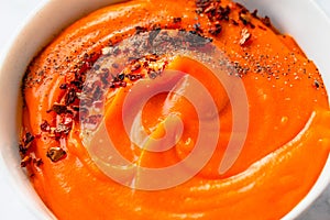 Roasted pumpkin and carrot soup with black and chili flakes pepper on marble background. Close-up