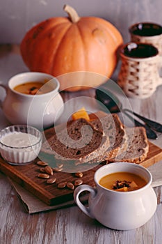 Roasted pumpkin and carrot soup with cream and pumpkin seeds on white wooden background. Copy space