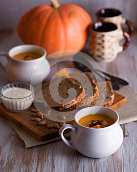 Roasted pumpkin and carrot soup with cream and pumpkin seeds on white wooden background. Copy space