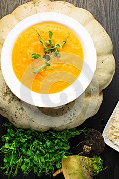 Roasted pumpkin and carrot soup with cream,turnip, pea tendrils, parsley on wooden background. Copy space