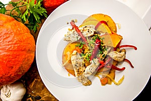 Roasted pumpkin and chicken meat on a white plate, top view