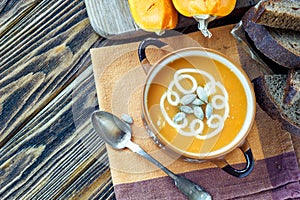 Roasted pumpkin soup with cream, fresh pumpkins and pumpkin seeds in plate on wooden background. Copy space
