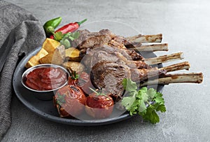 Roasted rack lamb chops on a plate with red sauce potatoes and tomatoes