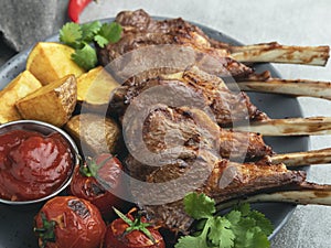 Roasted rack lamb chops on a plate with red sauce potatoes and tomatoes