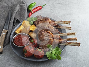 Roasted rack lamb chops on a wooden board with red sauce potatoes and tomatoes