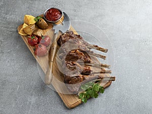 Roasted rack lamb chops on a wooden board with red sauce potatoes and tomatoes