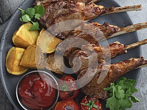 Roasted rack lamb chops on a wooden board with red sauce potatoes and tomatoes