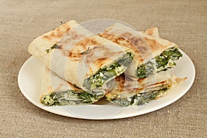 Roasted rolls of bread lavash filled with herbs and feta cheese at white plate on rough linen cloth. Closeup