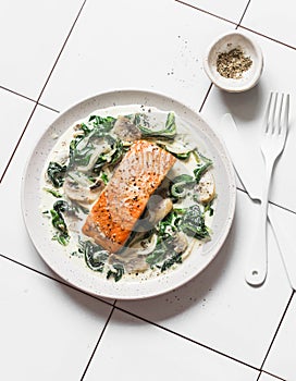 Roasted salmon with creamy spinach mushrooms sauce on a light background, top view. Salmon florentine photo