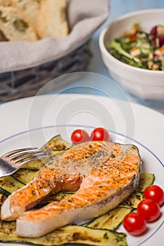 Roasted salmon and green zucchini with vvegetables salad in background