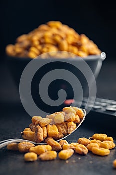 Roasted salted corn snack in spoon on black table