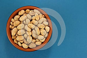 Roasted salted peanuts in bowl on blue background, top view