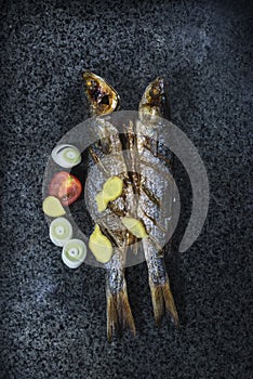 Roasted saury and cut tomatoes on slate background
