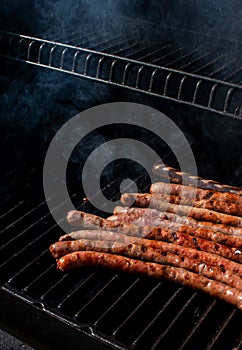 Roasted sausages cooking on flaming grill barbecue with smoke.